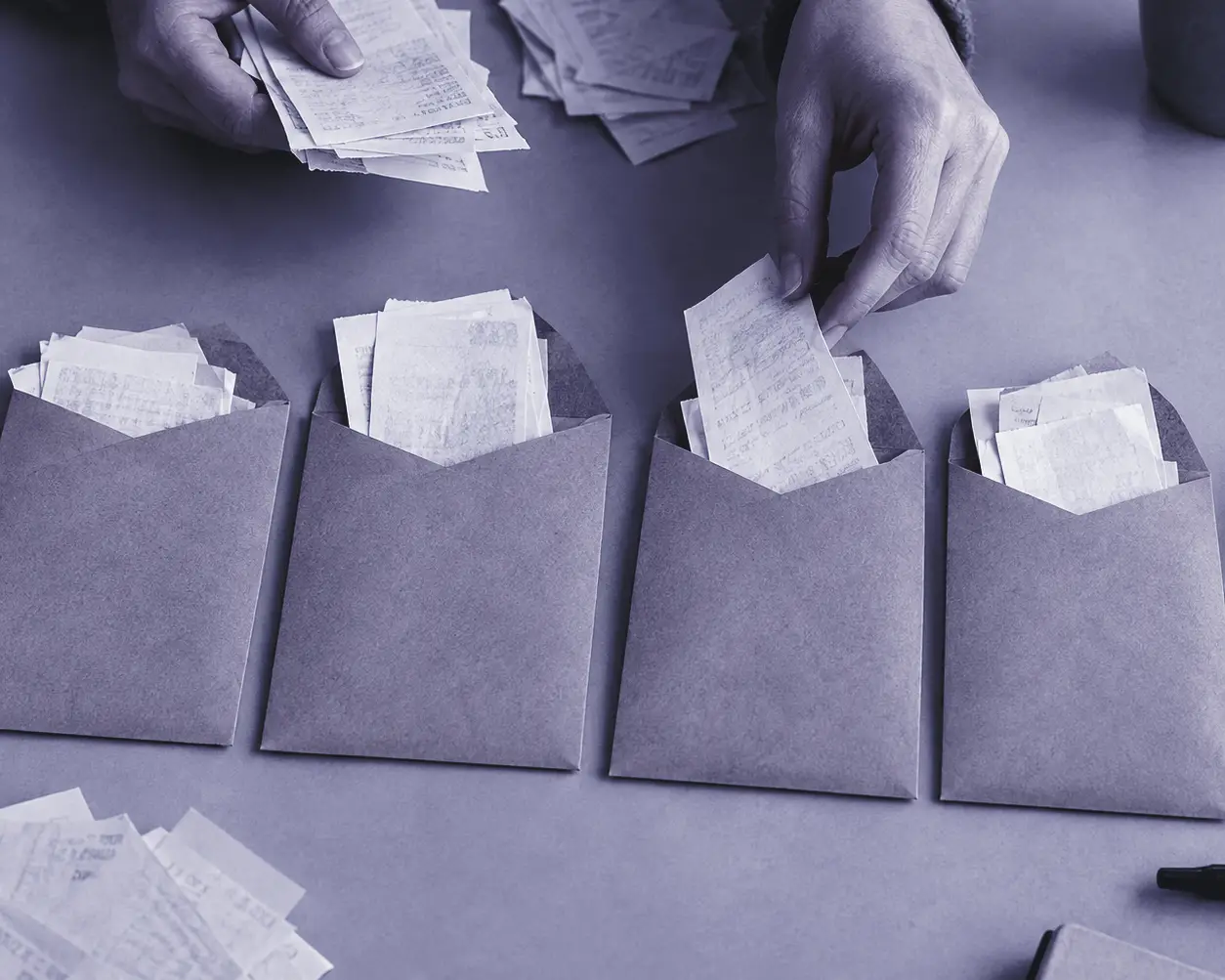 Manos repartiendo tiques de compra en cuatro sobres de papel kraft sobre una mesa gris